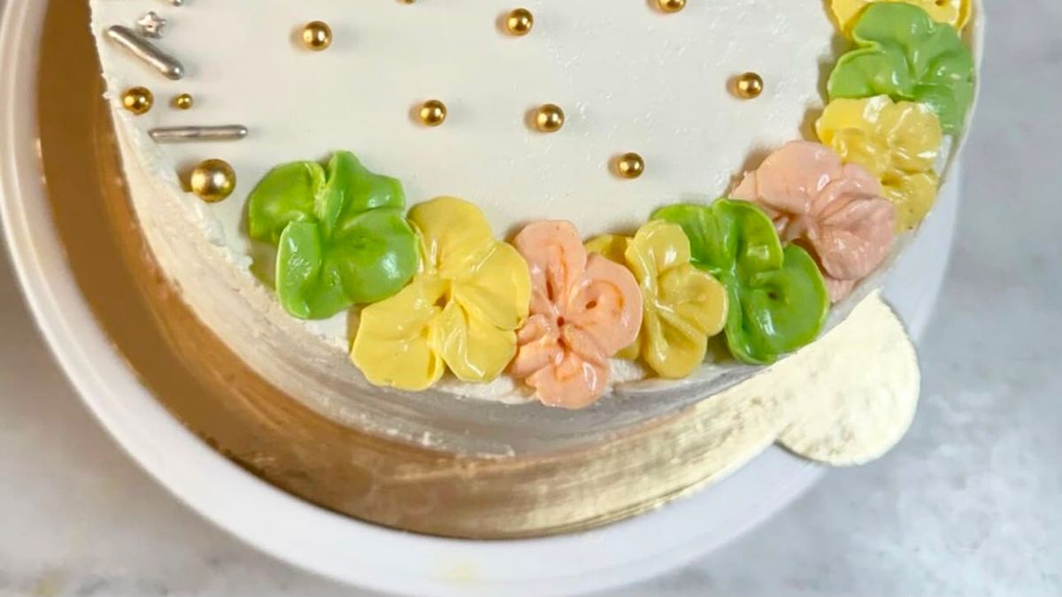 Beyaz pasta; altın drajeler ve pastel krema çiçeklerle süslenmiş