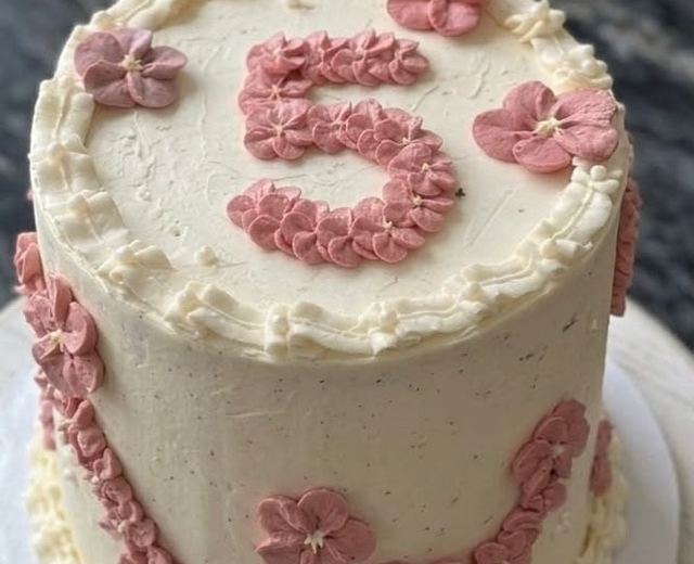Cremefarbene Geburtstagstorte mit einer Fünf aus rosa Spritzblüten